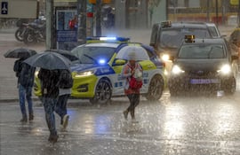 Varias personas se protegen de la lluvia en la Plaza de España de Barcelona. Este martes siguen en alerta naranja.