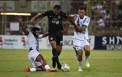 Ramón Martínez (c), futbolista de Olimpia, pelea por el balón en medio de dos rivales en el partido frente a Sportivo Ameliano por el torneo Apertura 2024 del fútbol paraguayo en el estadio Villa Alegre, en Encarnación.
