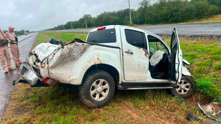 Dos agentes en uniforme de camuflaje junto a una camioneta ISUZU blanca accidentada en una carretera rodeada de árboles.
