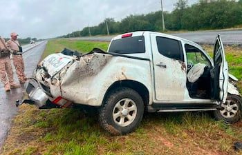Dos agentes en uniforme de camuflaje junto a una camioneta ISUZU blanca accidentada en una carretera rodeada de árboles.
