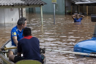Personas en un bote observan a un hombre caminando por una zona inundada este domingo, en la ciudad de Porto Alegre (Brasil).