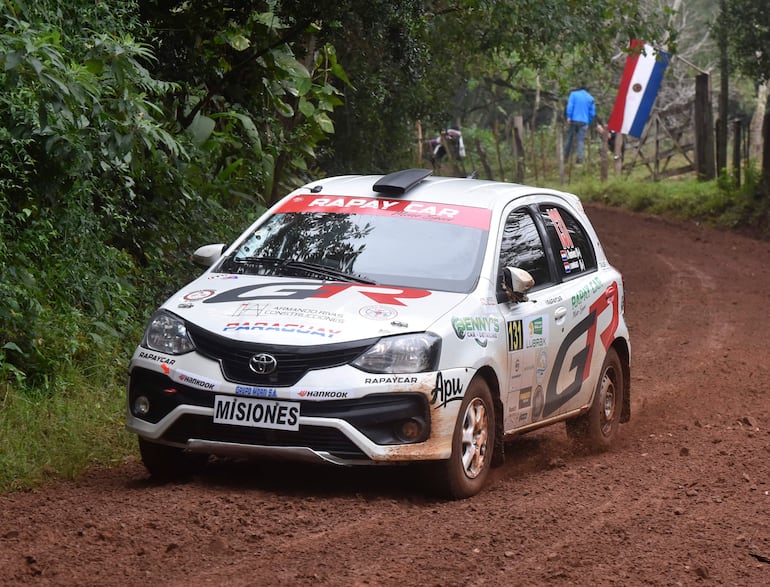 Un automóvil Toyota de rally atraviesa un camino de tierra con vegetación abundante a los lados.