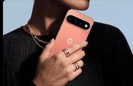 Mujer con blusa negra y joyas sostiene un teléfono rosa de la marca 'G' en fondo azul claro.