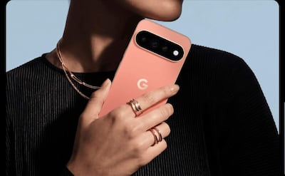 Mujer con blusa negra y joyas sostiene un teléfono rosa de la marca 'G' en fondo azul claro.