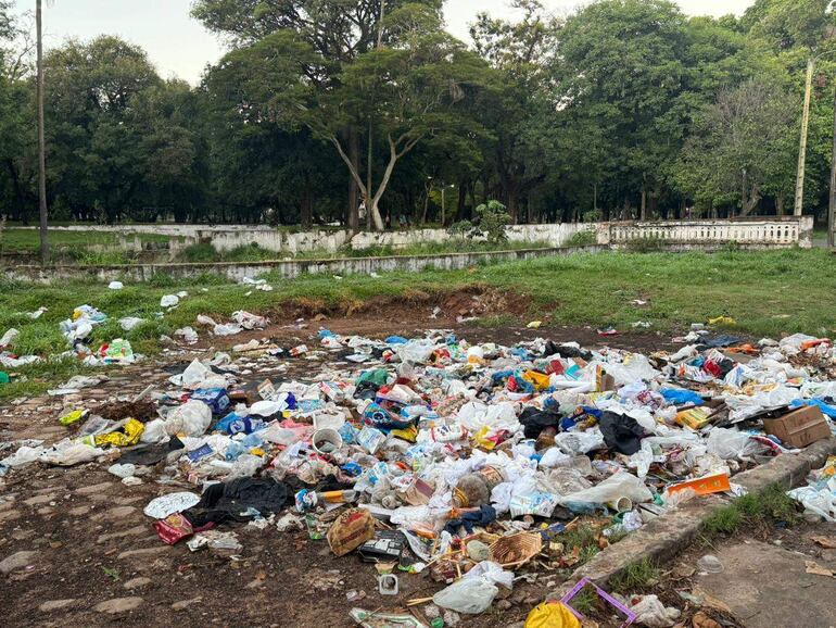 Parque Caballero desierto, con gran cantidad de basura acumulada en el suelo, rodeado de árboles y una pared blanca al fondo.