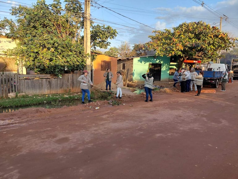 Mujer liderando limpieza con garabato, rodeada de personas en chaquetas claras y jeans, en una calle arbolada y colorida.