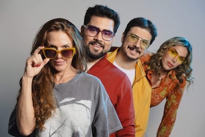 Mujer con gafas de sol amarillas y cabello rizado sonríe, acompañada de tres personas con diferentes gafas y atuendos coloridos.