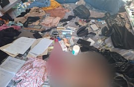 Entorno desordenado con ropa y documentos dispersos sobre una cama deshecha en la casa de Ariel Morán.