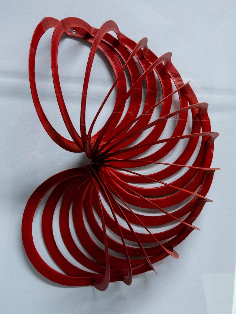 Escultura abstracta roja con diseño en espiral, ubicada en un ambiente blanco y neutro.
