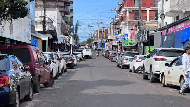 Calle urbana en Encarnación con vehículos estacionados y un hombre caminando, en un día despejado.