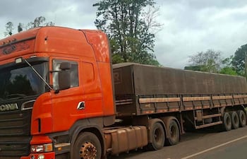 Camión Scania naranja estacionado en carretera, sin personas visibles, rodeado de árboles y cielo nublado.