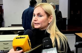 Ana Elizabeth Girala López con cabello rubio largo, en suéter negro, habla frente a varios micrófonos en una sala de conferencias.