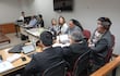 Mikhaela Rolón en blusa clara, lee una carta, mientras dos hombres con traje la observan en audiencia formal.
