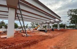 Sitio de construcción con trabajadores en chalecos de seguridad, columnas y grúa en un día nublado.
