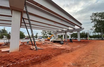 Sitio de construcción con trabajadores en chalecos de seguridad, columnas y grúa en un día nublado.