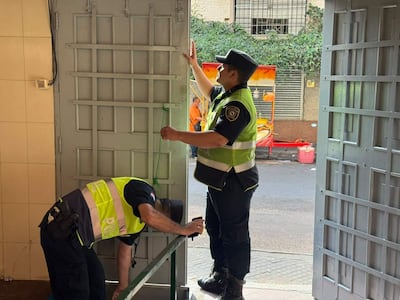 Dos agentes de policía en uniforme, uno arrodillado y otro de pie, manipulando rejas en un entorno urbano.