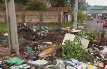 Montículos de basura, incluyendo cubiertas y restos de ropa, en un ambiente descuidado de un patio baldío sin personas visibles.