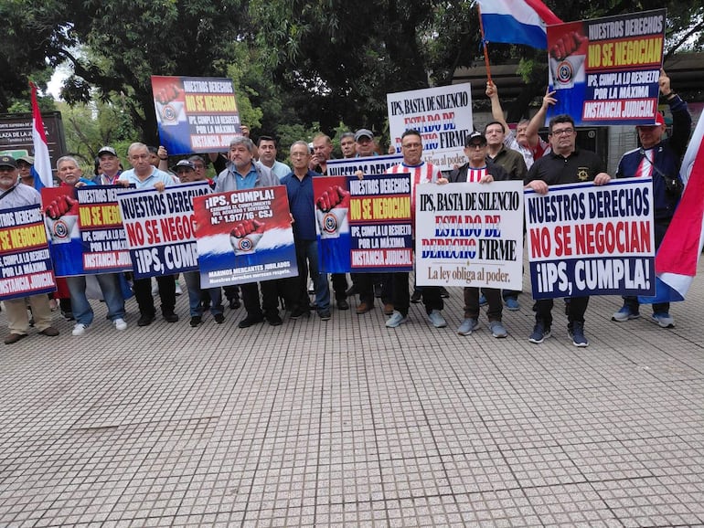 Grupo de manifestantes con carteles que dicen 'Nuestros derechos no se negocian' y 'IPS, cumpla!', en un ambiente de protesta pacífica.