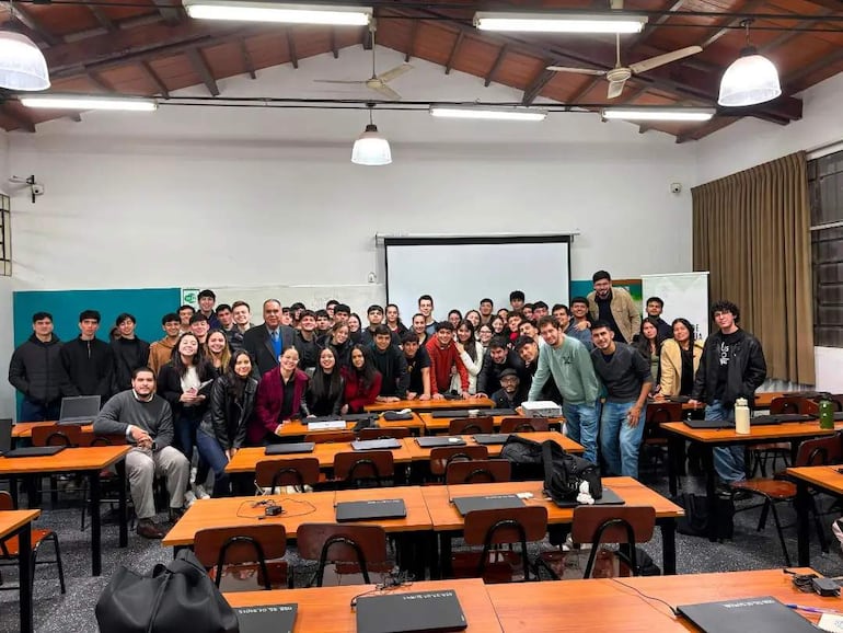 Grupo de estudiantes de la UNA en aula, vestidos casualmente, algunos sonríen mientras se posan para la fotografía.