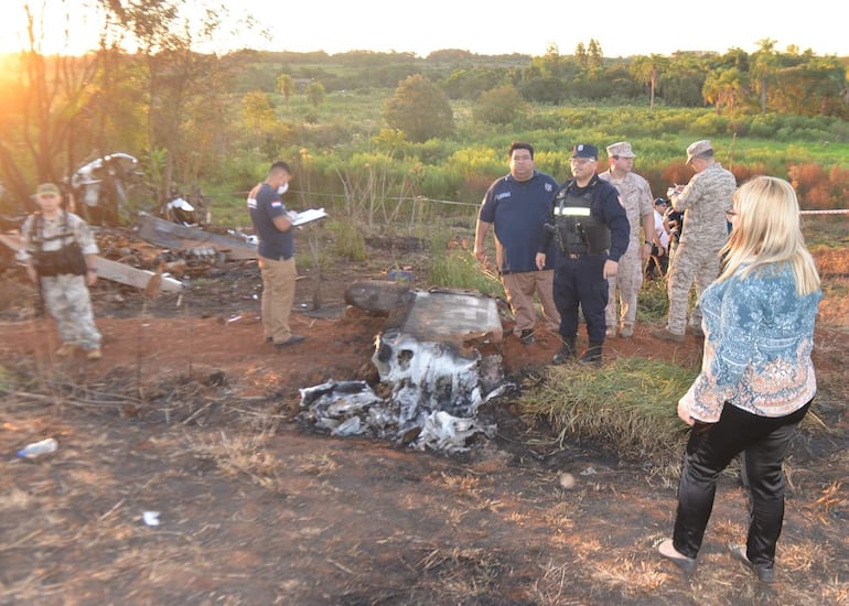 Hombres y mujeres analizan el lugar del accidente, uno con chaleco táctico y otro tomando notas, entre restos de un vehículo.