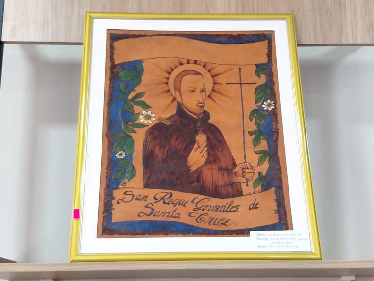 Retrato de San Roque González de Santa Cruz en marco amarillo, con hojas verdes y flores al fondo.