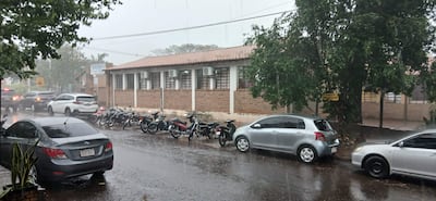 Escena urbana con coches y motocicletas estacionadas bajo lluvia intensa y cielo nublado.