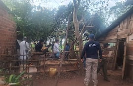 Hombres en uniforme policial y camisa blanca en área rural, investigando en un entorno natural con árboles y vegetación.