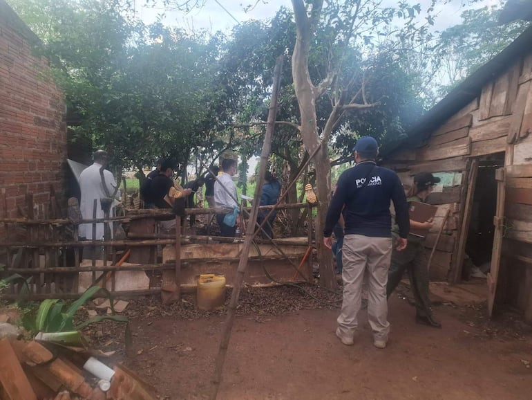Hombres en uniforme policial y camisa blanca en área rural, investigando en un entorno natural con árboles y vegetación.
