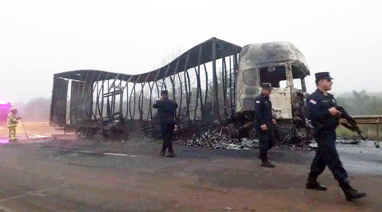 Policías aparecen frente al camión Scania de la empresa Estrella Express, que fue quemado luego de ser asaltado sobre la ruta PY07, en Canindeyú.