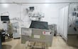 Cama de hospital con mantel gris y cartel de 'RIESGO ALTO DE CAÍDAS', rodeada de equipos médicos en un entorno vacío.
