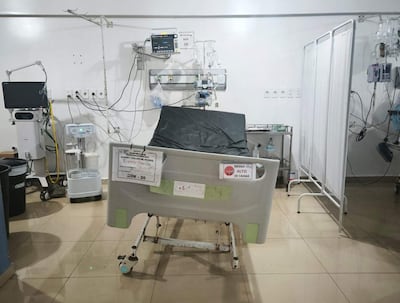 Cama de hospital con mantel gris y cartel de 'RIESGO ALTO DE CAÍDAS', rodeada de equipos médicos en un entorno vacío.