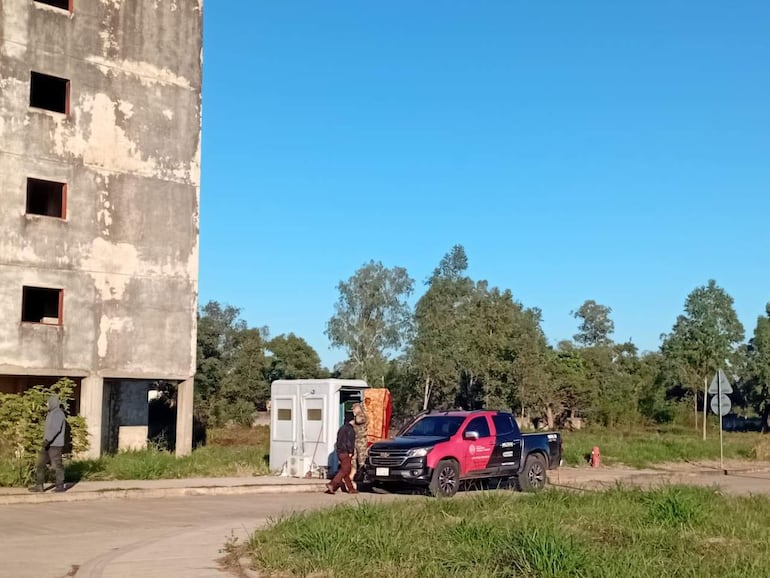 Dos personas caminan hacia un pick-up rojo y negro, rodeadas de un entorno natural en un área posiblemente en desuso.