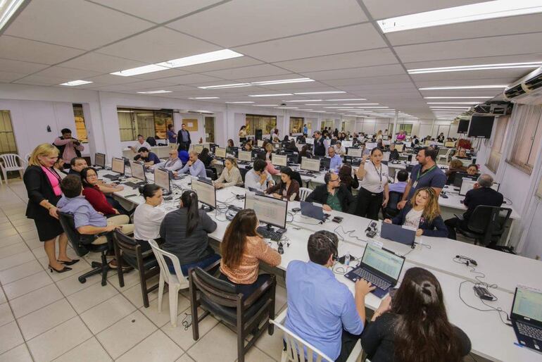 Cerca de 40 personas adultas trabajan en mesas con computadoras, mostrando actitudes de tranquilidad y colaboración en un ambiente ordenado.