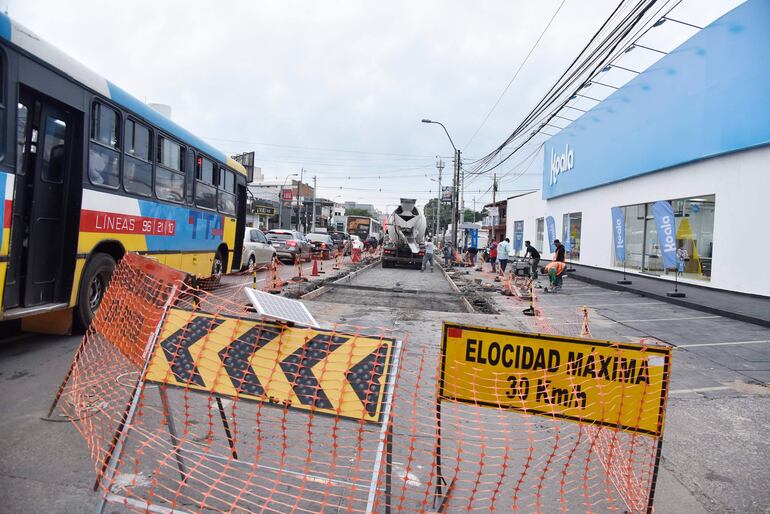 Obras en la avenida Eusebio Ayala, autobús de 'Líneas 96' en primer plano y trabajadores con vestimenta de seguridad en fondo difuso.