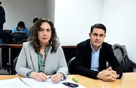 Alba Zaracho, con blusa de rayas verdes, conversa con Hernán Rivas, vestido con saco negro, en un ambiente formal.
