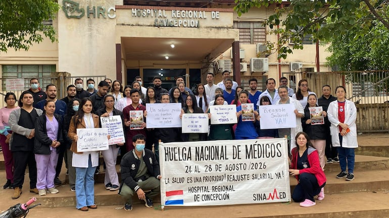 Médicos en batas blancas, verdes y moradas sosteniendo carteles con reclamos en un ambiente de protesta frente al hospital.