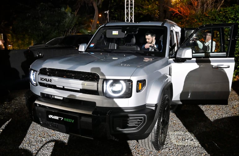 Hombre cerca de un SUV plateado en evento nocturno, observando atentamente el vehículo en exposición.