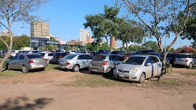 Numerosos vehículos desorganizados en la Plaza España, rodeados de vegetación, bajo un cielo despejado.
