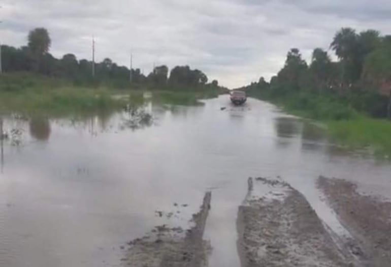 Vehículo en medio de un camino inundado rodeado de árboles y arbustos, bajo un cielo nublado en un entorno natural.