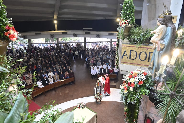 Sacerdote en vestimenta roja habla desde un atril, rodeado de una congregación atenta en un ambiente solemne decorado.