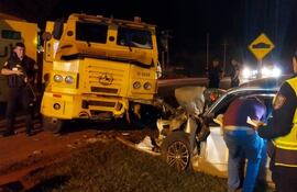 Policías en la escena del accidente, uno con arma, mientras observan un camión amarillo volcado y un coche blanco dañado.