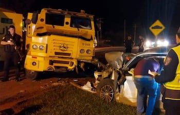 Policías en la escena del accidente, uno con arma, mientras observan un camión amarillo volcado y un coche blanco dañado.