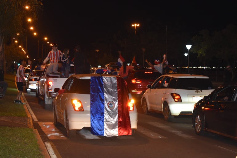 Hinchas en una camioneta con camiseta nacional, celebran agitando banderas en una calle iluminada durante la celebración nocturna.
