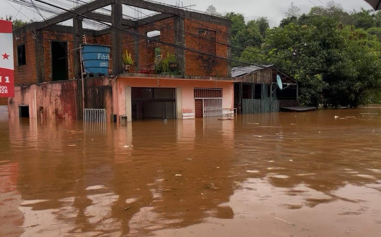 Edificio de ladrillo anaranjado parcialmente sumergido en agua, con cielo nublado en un ambiente de inundación.