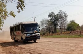 Autobús en movimiento levantando polvo en carretera rural, rodeado de árboles y paisaje poco desarrollado.
