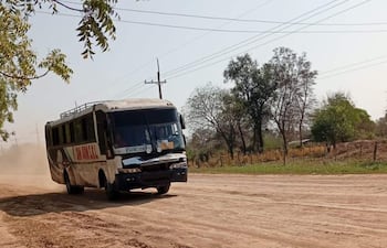 Autobús en movimiento levantando polvo en carretera rural, rodeado de árboles y paisaje poco desarrollado.