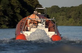 Embarcación naranja y blanca con dos personas en chalecos salvavidas navegando en aguas rodeadas de vegetación densa.