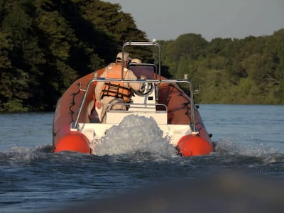 Embarcación naranja y blanca con dos personas en chalecos salvavidas navegando en aguas rodeadas de vegetación densa.