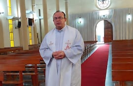 Sacerdote Ismael Obregón Olmedo, vestido con túnica blanca, de pie en el pasillo de una iglesia, con las manos juntas y mirando a la cámara.