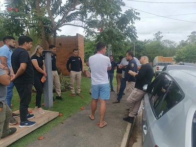Alfredo Rodríguez Rodríguez de espaldas, vestido con camiseta blanca y pantalones cortos, habla con oficiales de policía en un ambiente residencial.